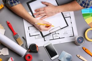 Manos de decorador con tablero, lápiz, muestras de color y herramientas para planificar una reforma