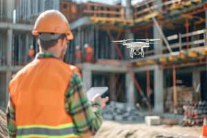 Técnico con chaleco naranja y casco manejando un dron para inspección de edificios